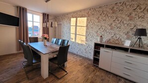 A modern dining area with a wooden table, black chairs, and a floral wallpaper. - Historic "Alter Bahnhof" Oberdorla with private playground, (Vogtei OT Oberdorla)