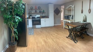 Cocina con armarios blancos, refrigerador y microondas. Hay una mesa de comedor con bancos y una planta colgante.