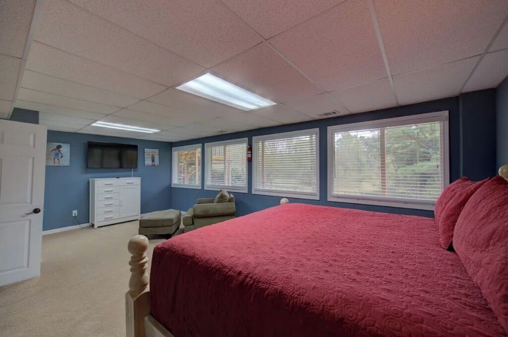 A bedroom with a large bed, a dresser, a chair, and a window with blinds.