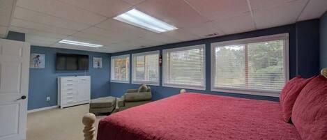 A bedroom with a large bed, a dresser, a chair, and a window with blinds.