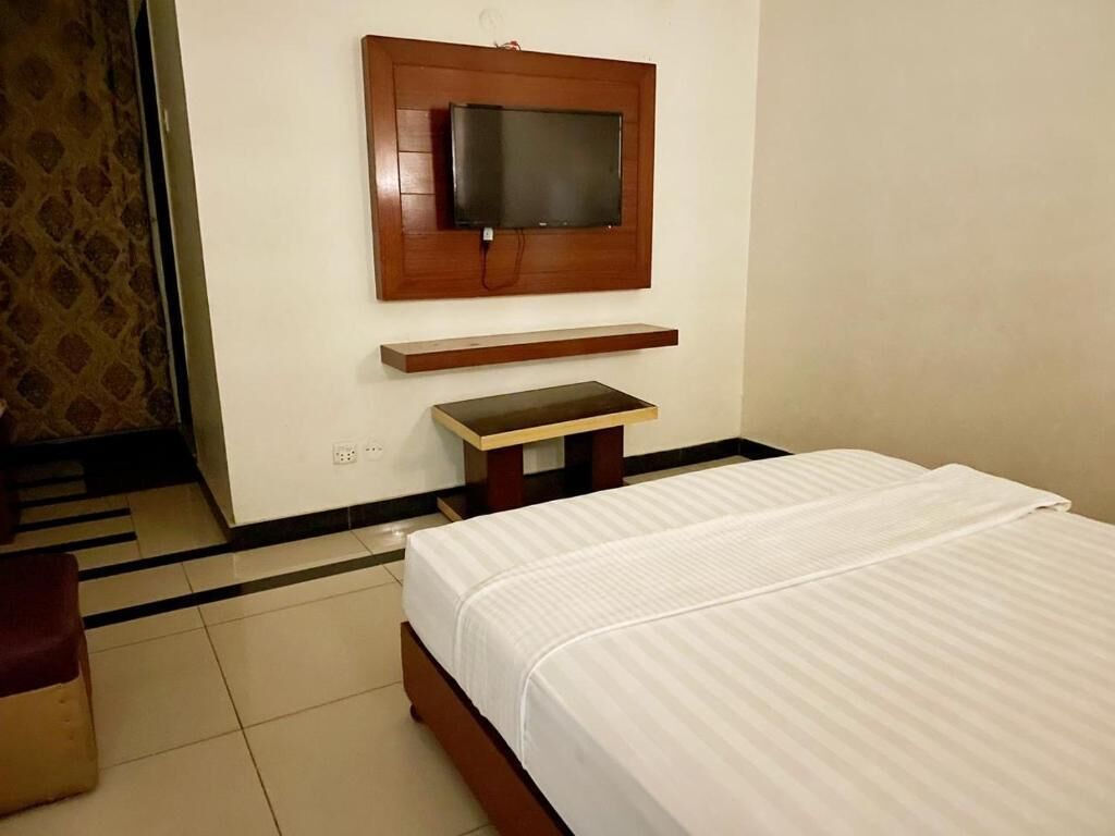 Una habitación de hotel con una cama, un televisor montado en la pared y una mesita.
