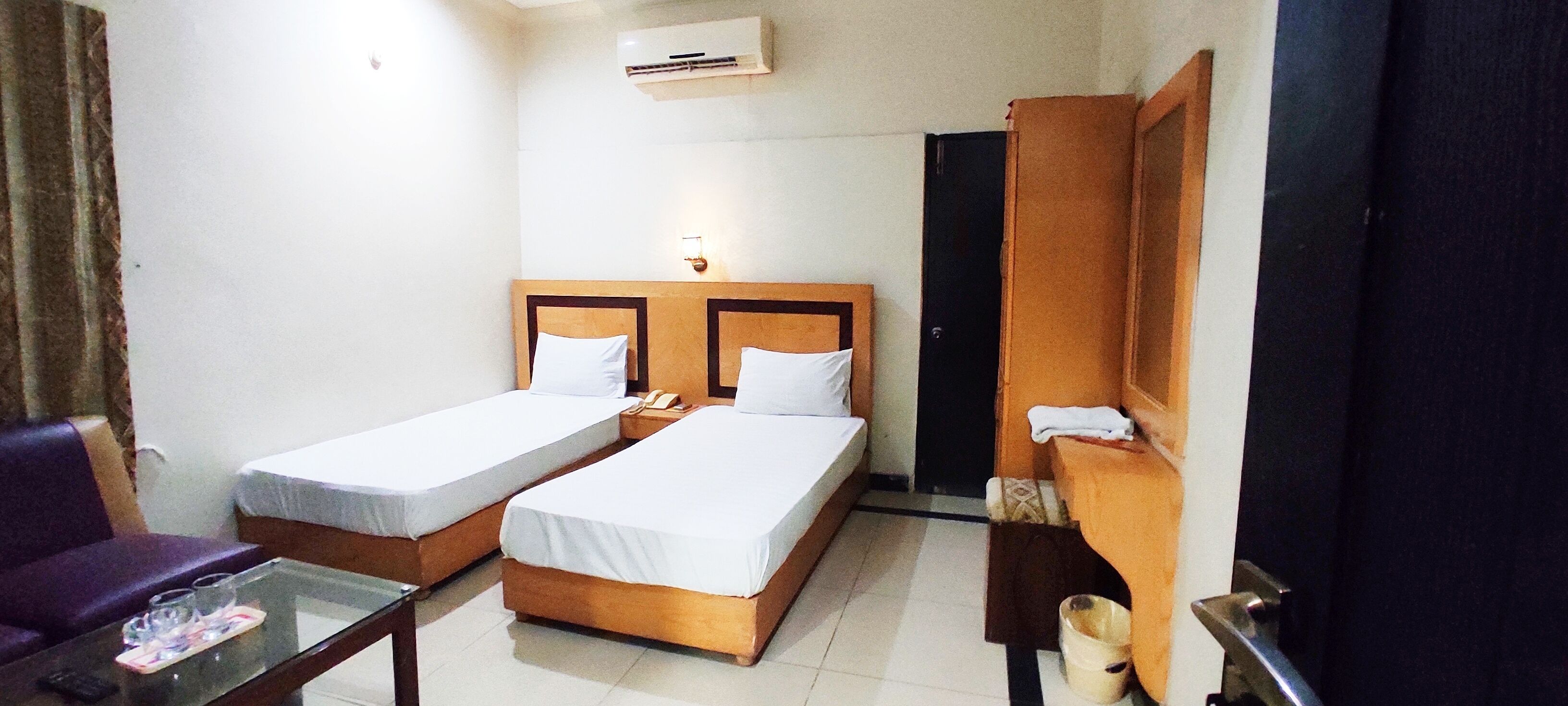 A hotel room with two single beds, a small table with a glass, a chair, and a wardrobe.