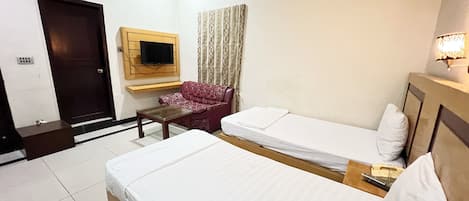 A hotel room with two single beds, a sofa, a TV mounted on the wall, and a small table.