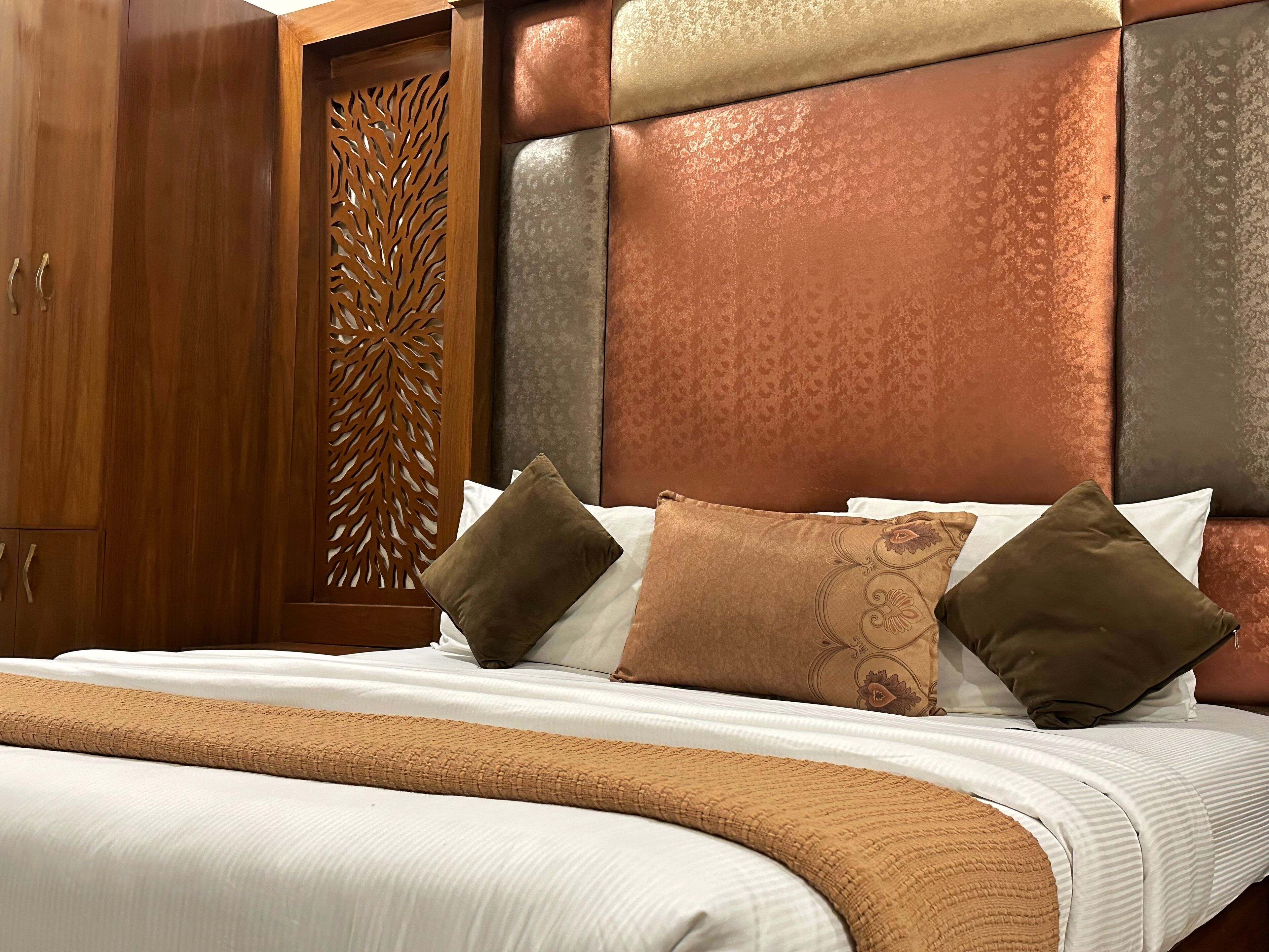 A neatly made bed with a patterned headboard, a wooden wardrobe, and a decorative panel.