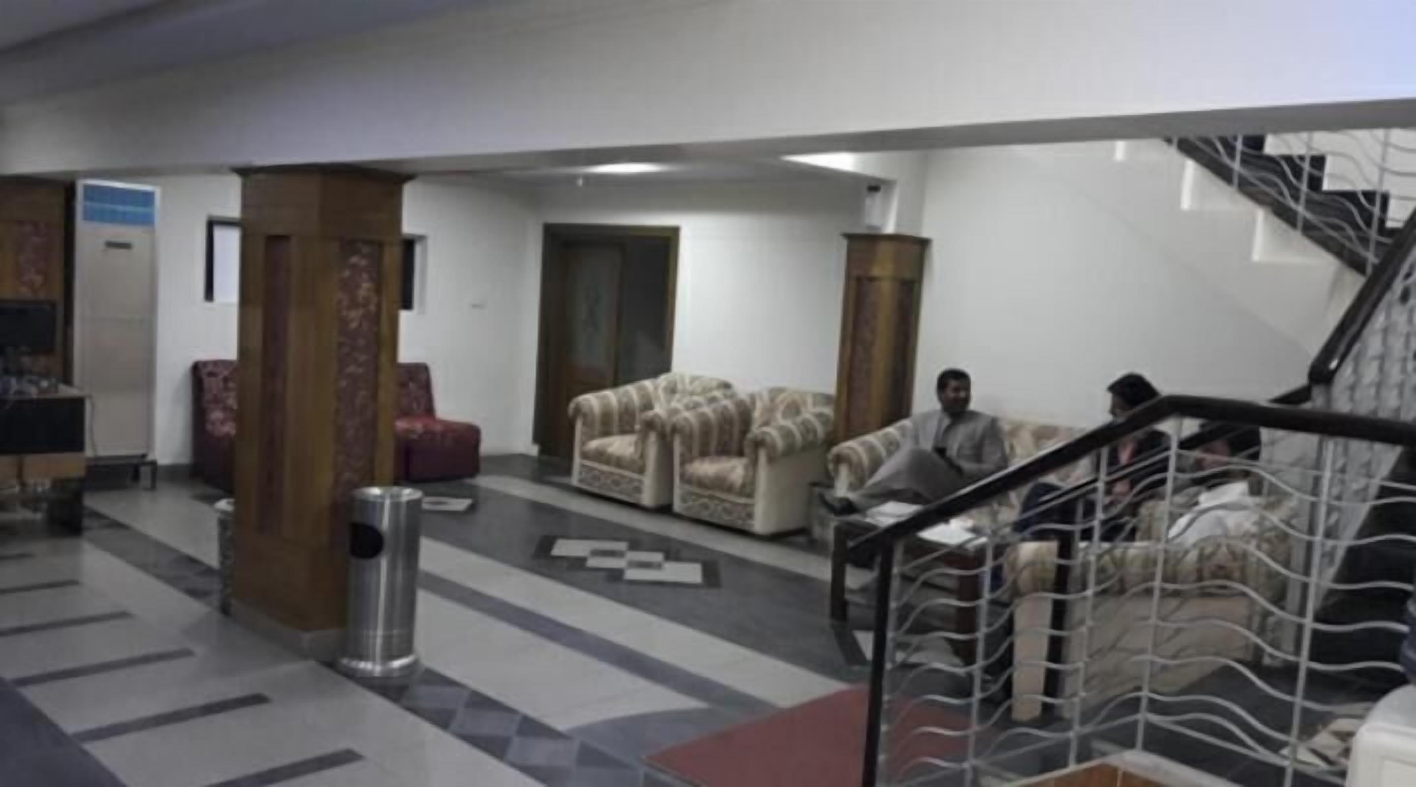 A lobby with a staircase, two sofas, a trash bin, and a patterned rug.