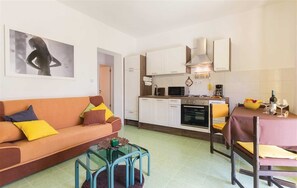A modern kitchen with white cabinets, a microwave, and a stove. There is a dining table with chairs and a sofa with cushions.