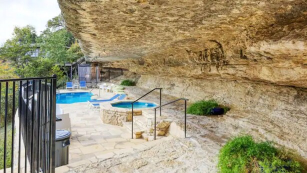 Un espace extérieur avec une piscine dont les parois sont recouvertes de pierres, agrémenté d’escaliers en pierre et de chaises longues.