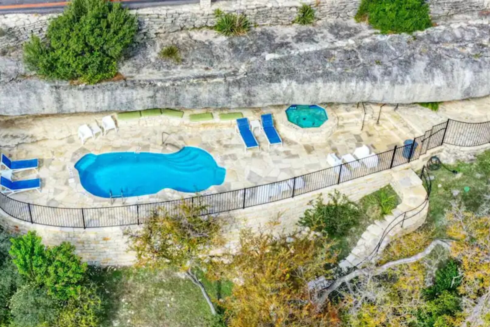 An aerial view of a swimming pool area with a large pool, several lounge chairs, and a small hot tub.