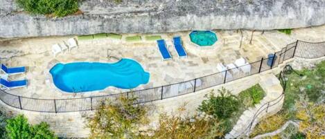 An aerial view of a swimming pool area with a large pool, several lounge chairs, and a small hot tub.