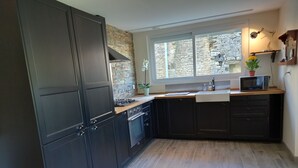 A modern kitchen with dark cabinetry, a stone backsplash, a window with a view, and a microwave on the countertop.