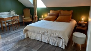 A bedroom with a large bed, a desk, a chair, and a small stool.