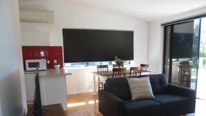 Una sala de estar moderna con un sofá oscuro, un televisor de pantalla plana y una mesa de comedor de madera.