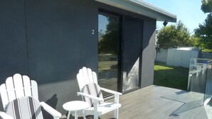 Un patio exterior moderno con sillas Adirondack blancas y una pequeña mesa redonda.