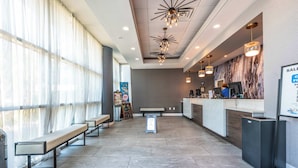En hotellobby med en receptionsdisk, sittplatser och ett stort fönster med gardiner.