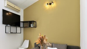 A modern living room with a round table, white chairs, a grey sofa, a mounted TV, and a wall-mounted shelf.