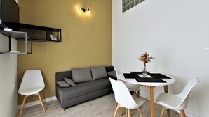 A modern living space with a grey sofa, white chairs, a small round table, and a vase with dried flowers.