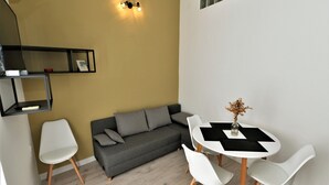 A compact living space with a grey sofa, white chairs, a small round table, and a wall-mounted shelf.