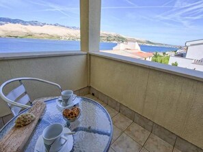 Un balcon avec une table, des chaises et une vue sur la mer et les collines.