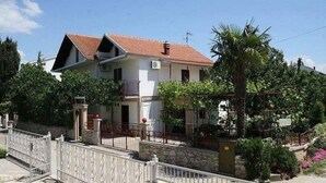 Une maison à deux étages, avec un toit recouvert de tuiles rouges, un balcon et une entrée fermée par un portail.