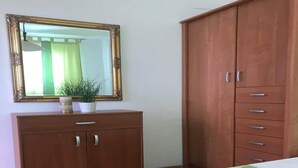 Une chambre avec une armoire en bois, une table de chevet, un miroir et une plante en pot.