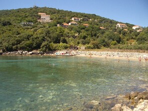 A coastal area with clear waters, a sandy beach, and buildings on a hillside. - Apartment Dario - One Bedroom Apartment with Terrace and Sea View (Gruda)