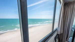 Ein Zimmer mit großem Fenster und Blick auf einen Strand.