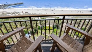 Un balcon avec des chaises en bois donnant sur une plage et une jetée.