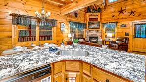 A wooden cabin interior with a large kitchen island, wooden cabinets, a fireplace, and a dining area. - 🏔🏔 180° Views 🏔🏔 ❸Decks ❸Masters ❷Game R♨Hot T (Sevierville)