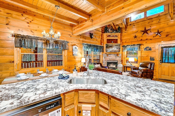 Interior de uma cabana de madeira com uma grande ilha na cozinha, armários de madeira, lareira e área de jantar.