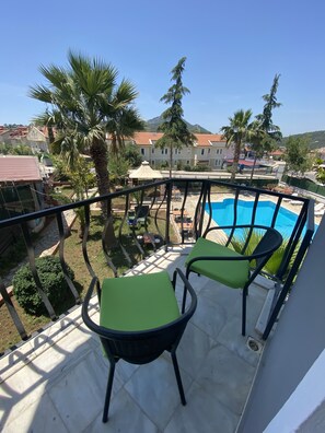 Un balcón con dos sillas verdes acolchadas, una piscina y palmeras circundantes.
