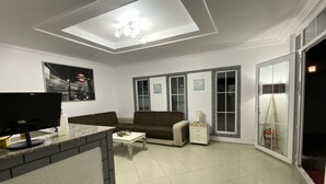 A living room with a flat-screen TV, a sofa, a coffee table, and a small side table. - Greenway Hotel (Fethiye)