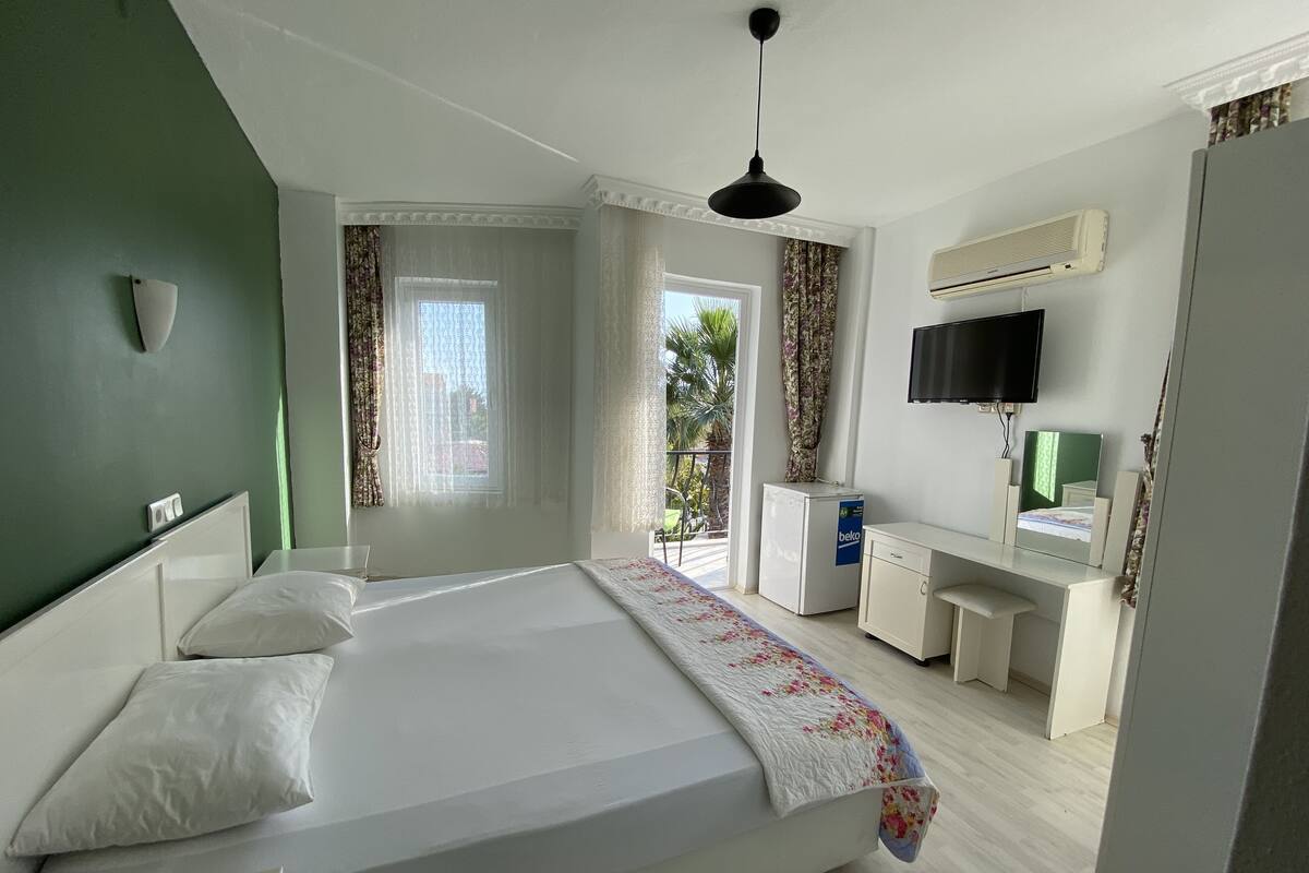A modern bedroom with a large bed, a desk, a television, and an air conditioning unit.