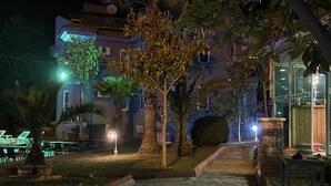 A nighttime outdoor area with a stone pathway, palm trees, and a building with a cafe sign. - Greenway Hotel (Fethiye)