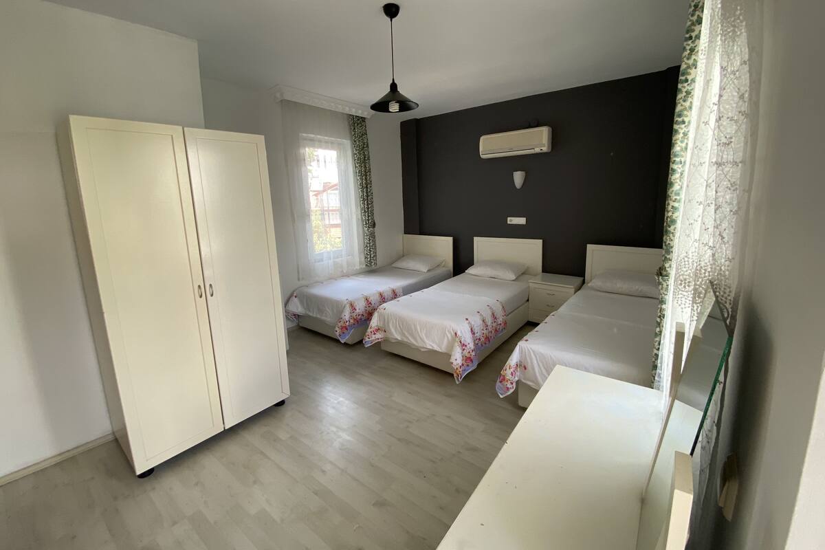 A bedroom with two single beds, a wardrobe, a ceiling fan, and a window with curtains.