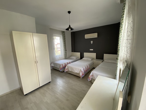 Un dormitorio con dos camas individuales, un armario, un ventilador de techo y una ventana con cortinas.