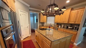 A kitchen with granite countertops, wooden cabinets, a central island, and a chandelier.