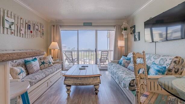 A spacious living room with a large sliding glass door leading to a balcony, furnished with a sofa, a coffee table, and a chair. - Captain's Cabana Gulf Front Condo (Galveston)