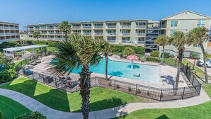 A hotel with a swimming pool surrounded by palm trees and a covered patio area. - Captain's Cabana Gulf Front Condo (Galveston)