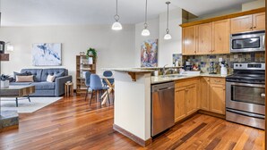 A modern kitchen with wooden cabinets, stainless steel appliances, and a central island. - Alluring Mountain View Condo - The Heart Of Downtown! (Canmore)