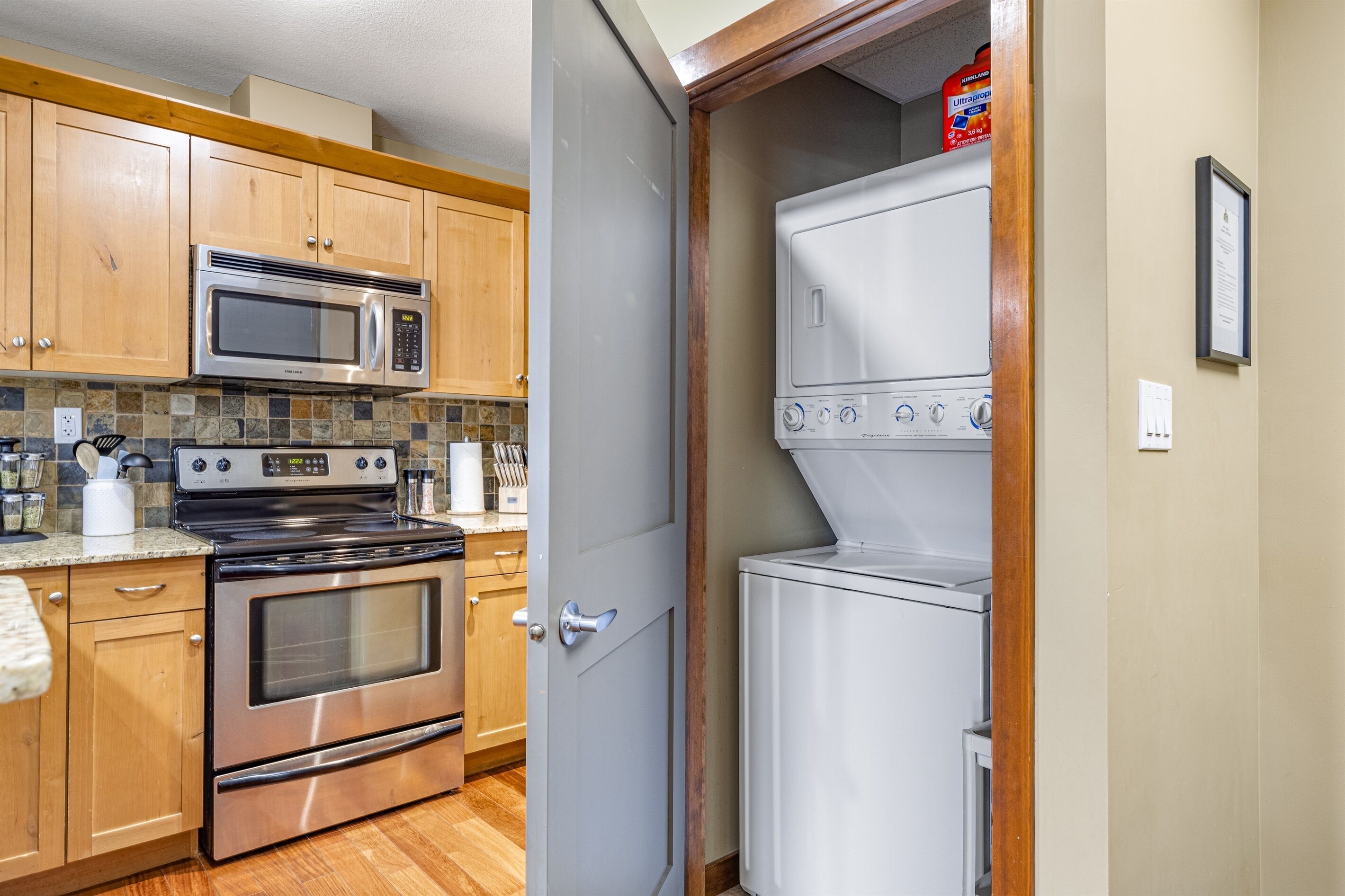 A kitchen with wooden cabinets, a stainless steel microwave, stove, oven, and a white washer and dryer.
