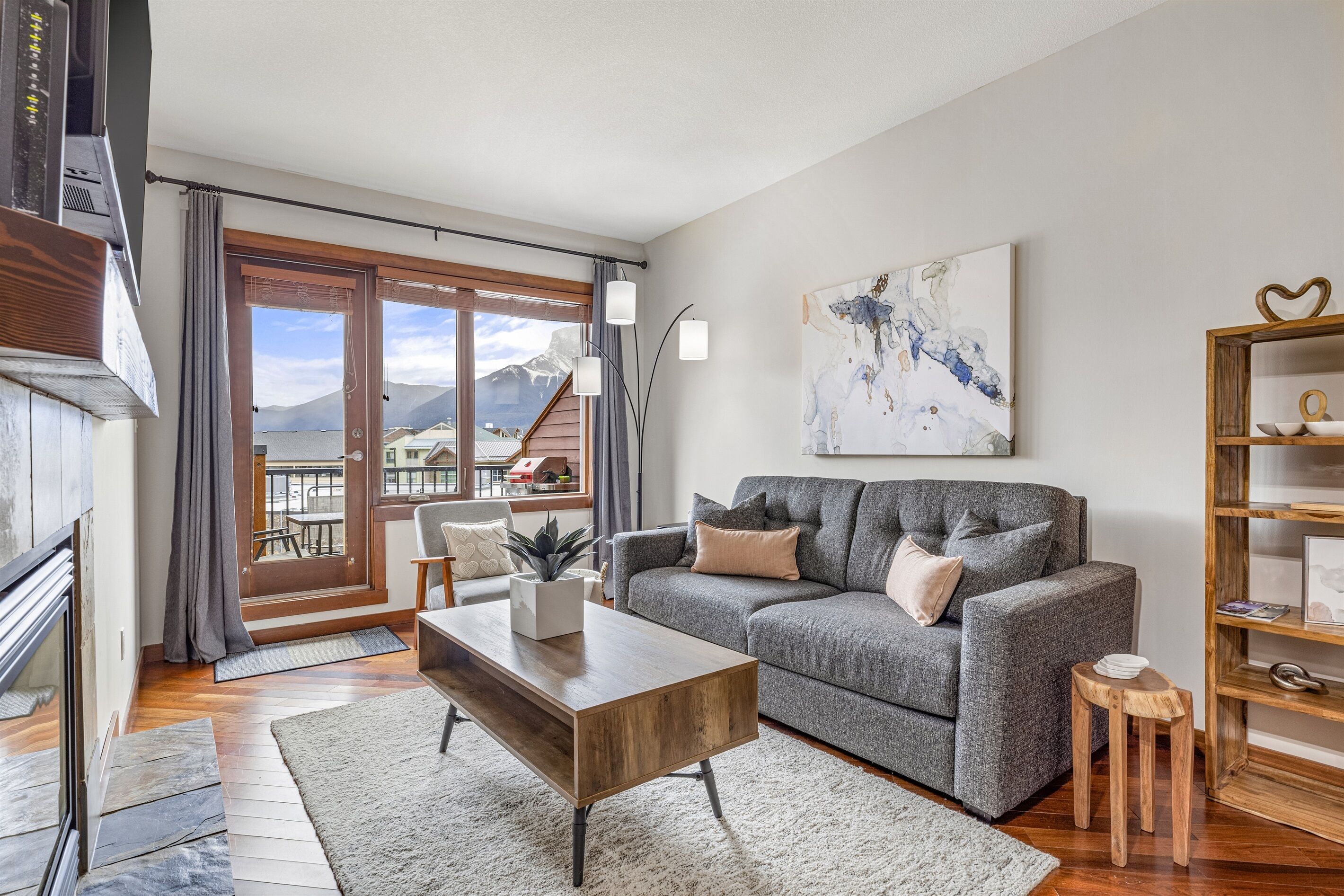 Een moderne woonkamer met een grijze bank, een houten salontafel en uitzicht op bergen door een schuifdeur van glas.