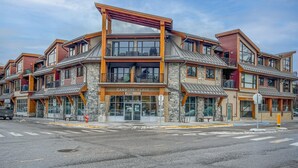 A multi-story hotel with a stone facade, large windows, and a prominent entrance. - Alluring Mountain View Condo - The Heart Of Downtown! (Canmore)