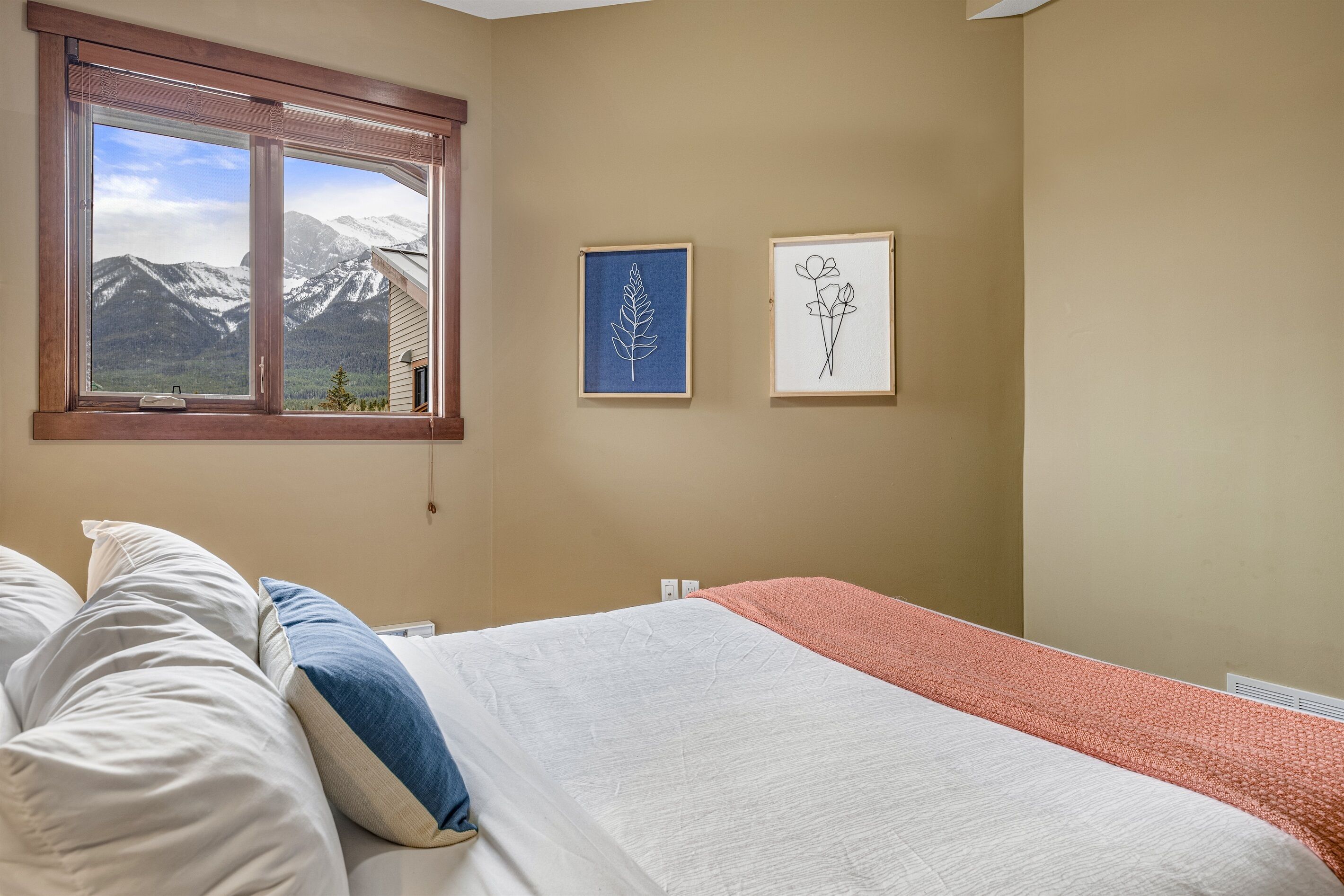 Quarto com cama, janela vista para montanhas e duas obras de arte emolduradas na parede.