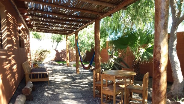 Un espace extérieur aménagé avec une table et des chaises, protégé par un auvent et entouré de verdure, avec un hamac à proximité.