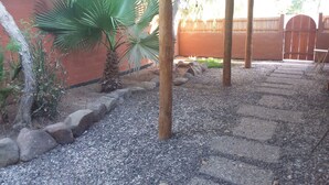Un patio couvert avec un chemin de gravier, des palmiers et une clôture en bois.