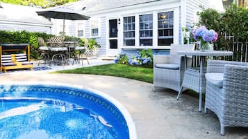 A backyard with a swimming pool, outdoor furniture, and a house with large windows.
