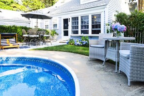 A backyard with a swimming pool, outdoor furniture, and a house with large windows. - Harbor Getaway Unit -1 (Harwich)
