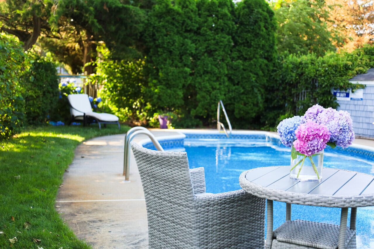 A swimming pool with a lounge chair and a table with a vase of flowers.