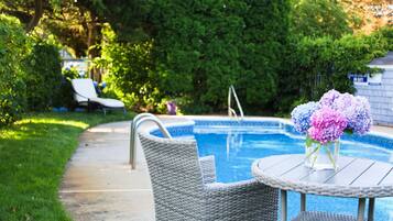 A swimming pool with a lounge chair and a table with a vase of flowers.