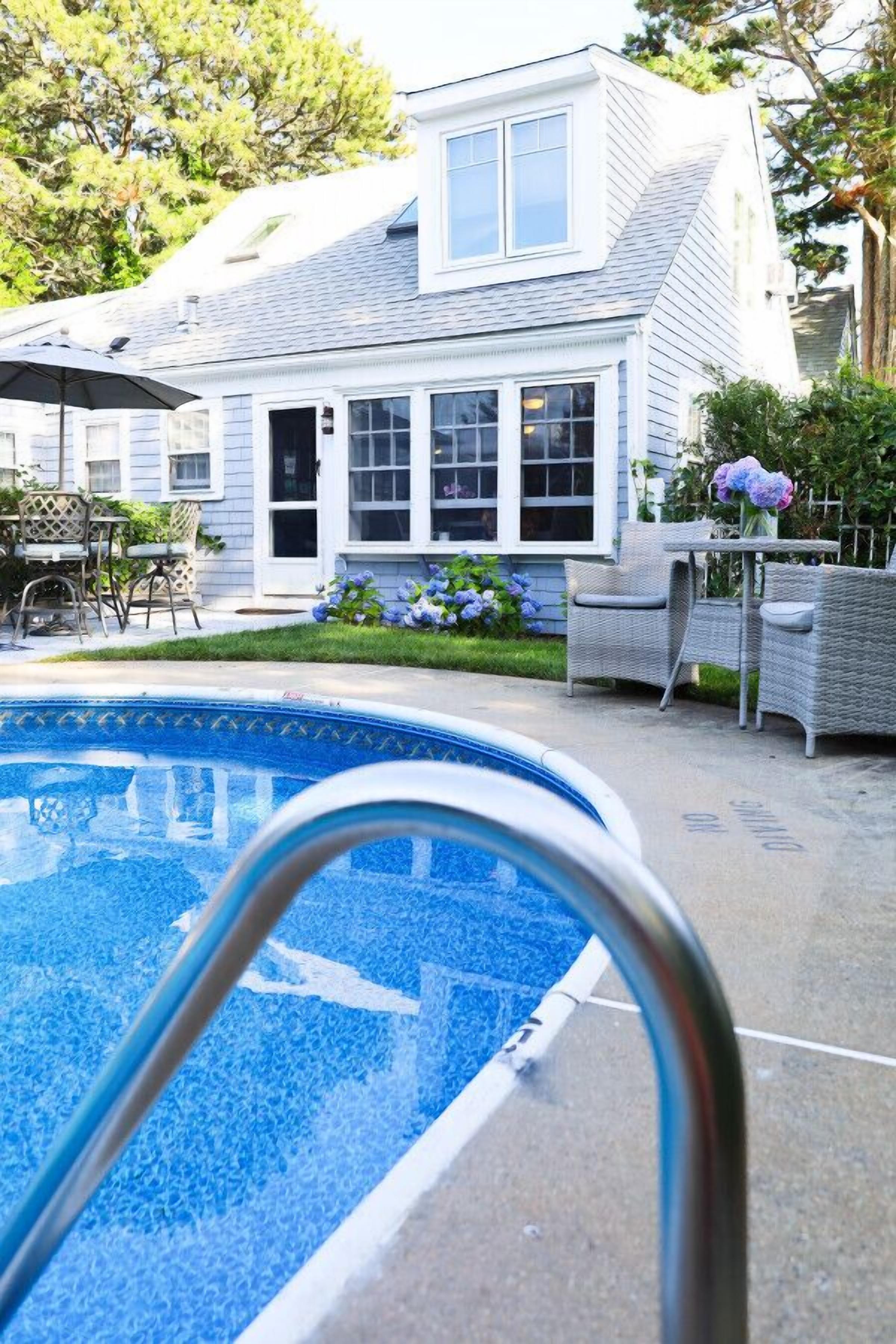 A residential backyard with a swimming pool, a patio with outdoor furniture, and a house with multiple windows and a covered porch.